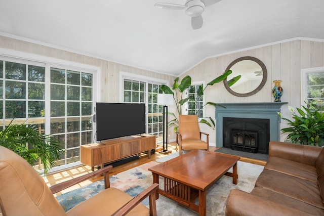 living area with wood finished floors, vaulted ceiling, a ceiling fan, a fireplace with flush hearth, and crown molding