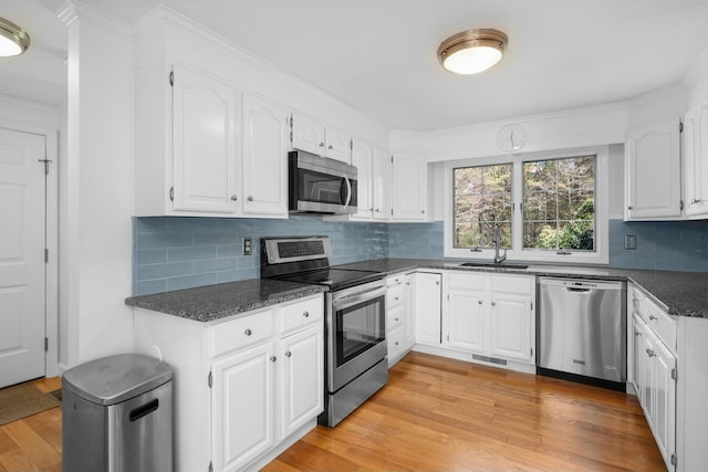 kitchen featuring appliances with stainless steel finishes, light wood finished floors, a sink, white cabinetry, and visible vents
