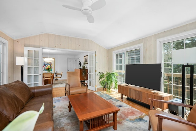 living area with wood finished floors, a ceiling fan, wooden walls, french doors, and lofted ceiling