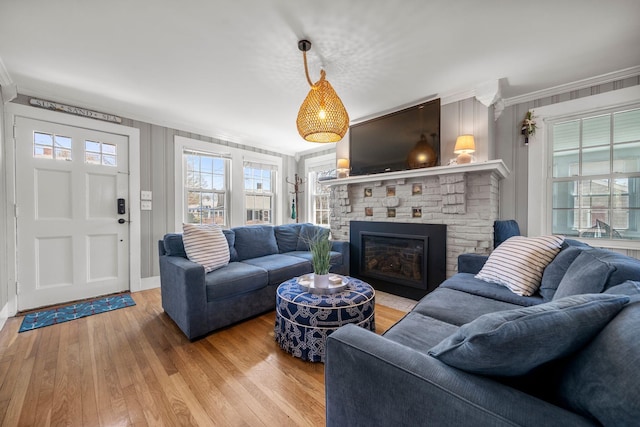 living room with ornamental molding, healthy amount of natural light, a glass covered fireplace, and light wood-style flooring