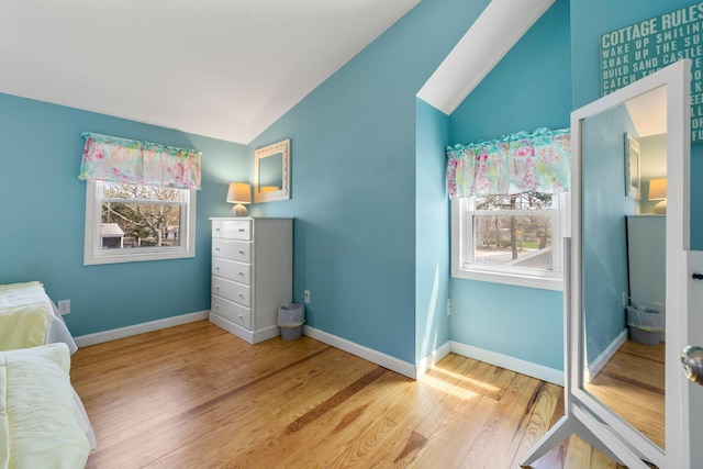 bedroom featuring lofted ceiling, multiple windows, wood finished floors, and baseboards