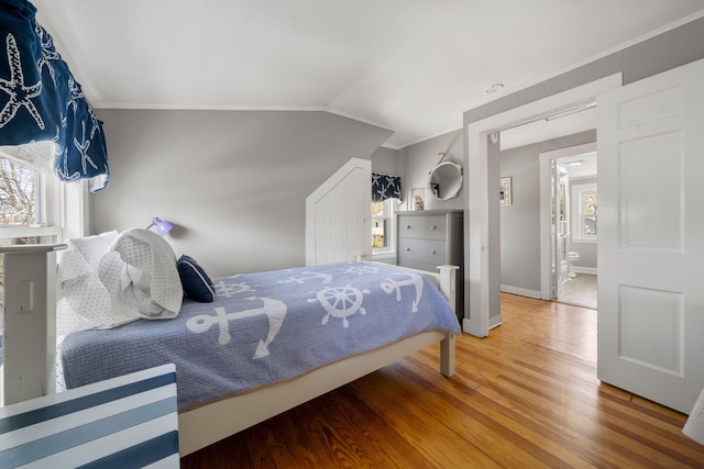 bedroom with wood finished floors, baseboards, ornamental molding, and lofted ceiling