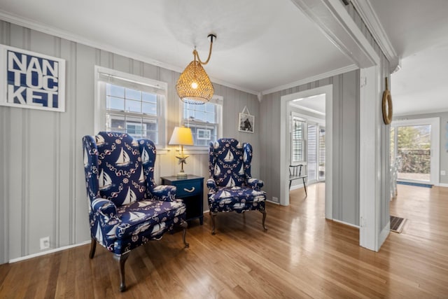 sitting room with ornamental molding, wood finished floors, a decorative wall, and baseboards