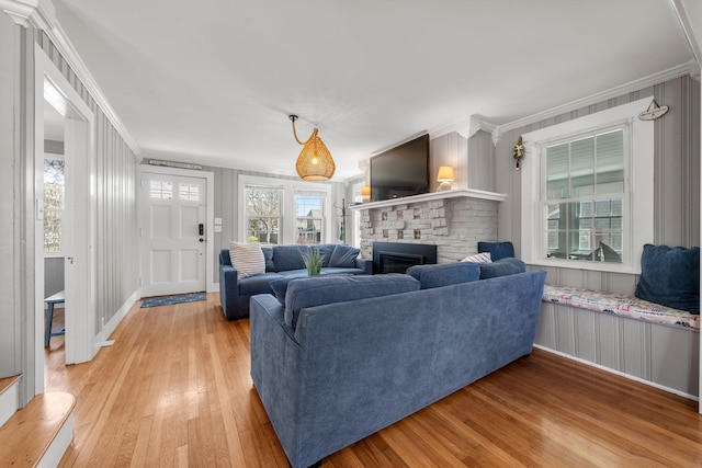 living room with light wood-type flooring, crown molding, a glass covered fireplace, a decorative wall, and baseboards