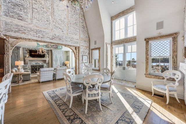 dining area featuring a towering ceiling, a fireplace, hardwood / wood-style floors, and a notable chandelier