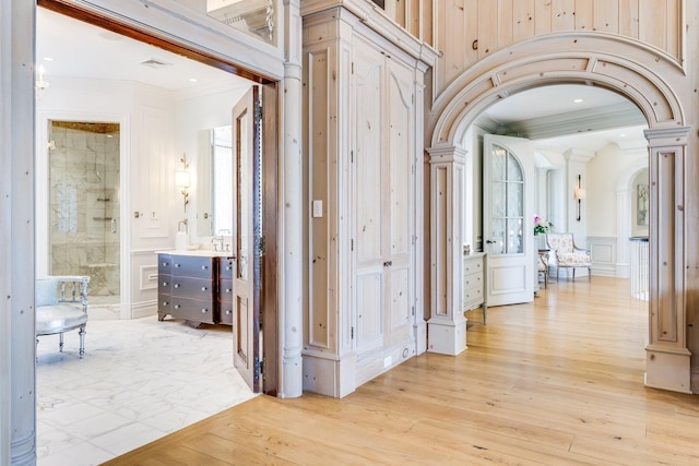 hallway featuring ornate columns, crown molding, and light wood-type flooring