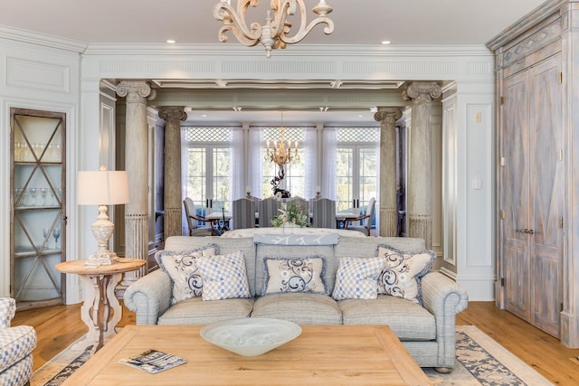 living room featuring ornate columns, crown molding, and an inviting chandelier