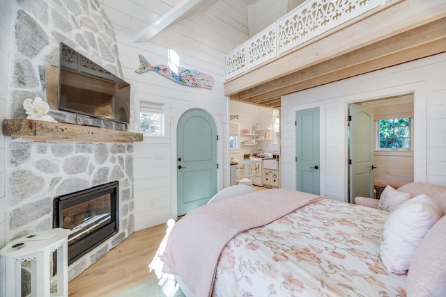 bedroom with a stone fireplace, light wood-type flooring, multiple windows, and wood walls