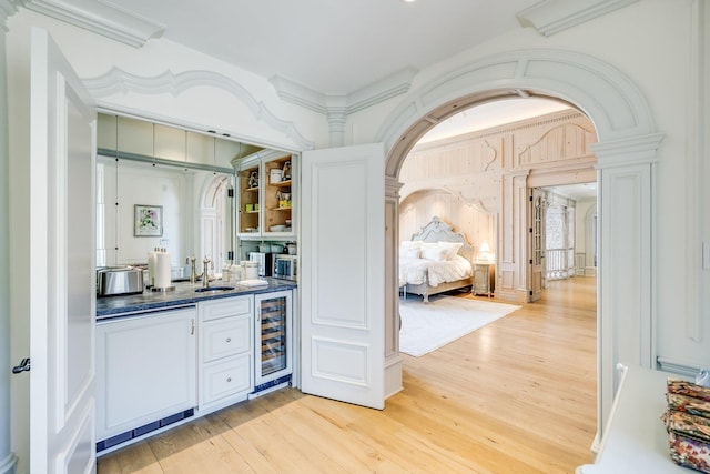 bar featuring sink, white cabinets, beverage cooler, crown molding, and light hardwood / wood-style flooring