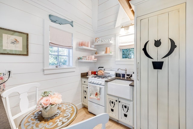 kitchen with sink, light hardwood / wood-style flooring, gas range gas stove, and wood walls