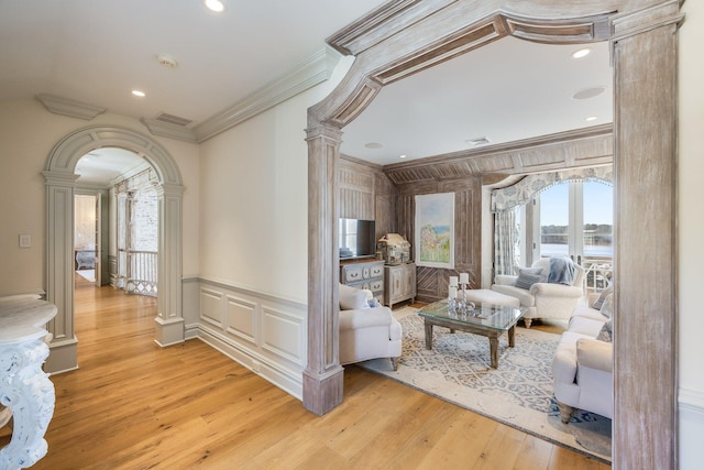 living room with decorative columns, ornamental molding, and light hardwood / wood-style floors