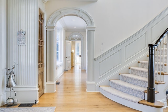 entrance foyer with crown molding, decorative columns, and light wood-type flooring