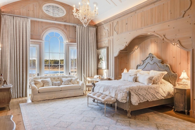 bedroom with a high ceiling, an inviting chandelier, wooden walls, and light hardwood / wood-style floors