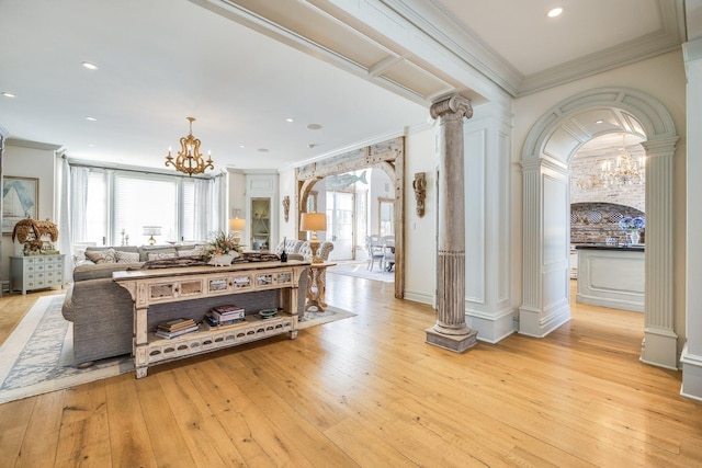 interior space featuring an inviting chandelier, decorative columns, ornamental molding, a healthy amount of sunlight, and light wood-type flooring