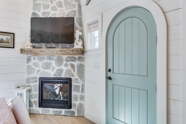 unfurnished living room featuring a stone fireplace, light hardwood / wood-style floors, and wood walls