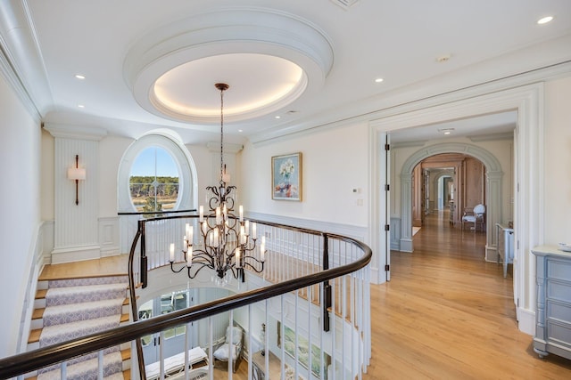 corridor with an inviting chandelier, light hardwood / wood-style flooring, ornamental molding, and a raised ceiling