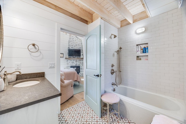 bathroom featuring beam ceiling, vanity, a stone fireplace, wooden ceiling, and tiled shower / bath