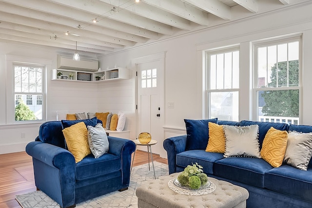 living area with beamed ceiling, a healthy amount of sunlight, light wood-style flooring, and a wall mounted AC