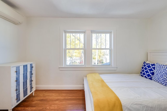 bedroom with a wall mounted air conditioner, baseboards, and wood finished floors