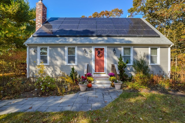 view of front facade with roof mounted solar panels, a chimney, and a shingled roof