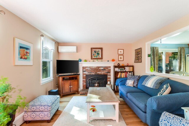 living area with a brick fireplace, a wall mounted AC, and wood finished floors