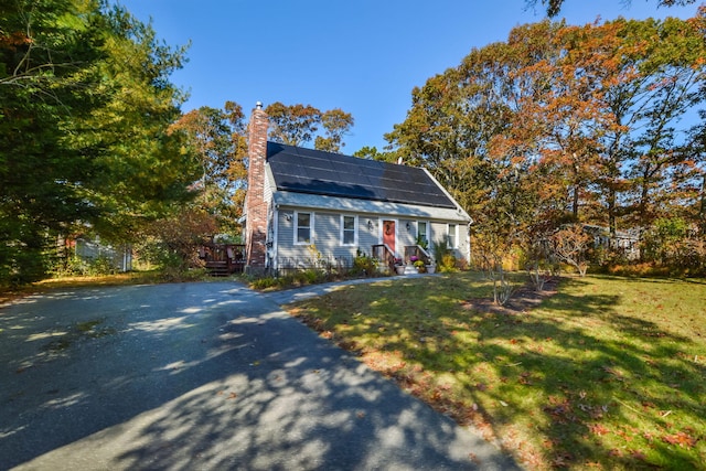 colonial inspired home with a chimney, solar panels, and a front yard