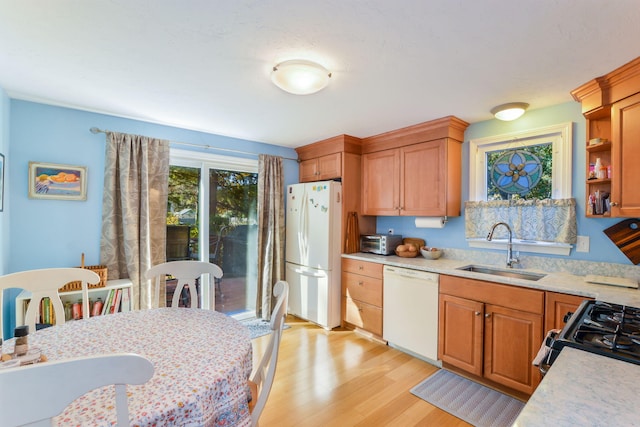 kitchen featuring light wood-type flooring, light countertops, brown cabinetry, white appliances, and a sink