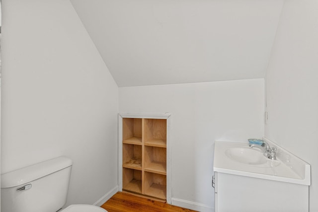 bathroom featuring wood-type flooring, toilet, vaulted ceiling, and vanity