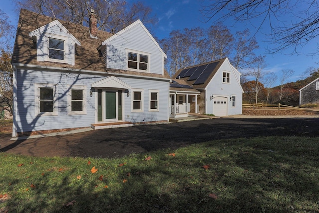 new england style home featuring covered porch, a garage, a front yard, and solar panels