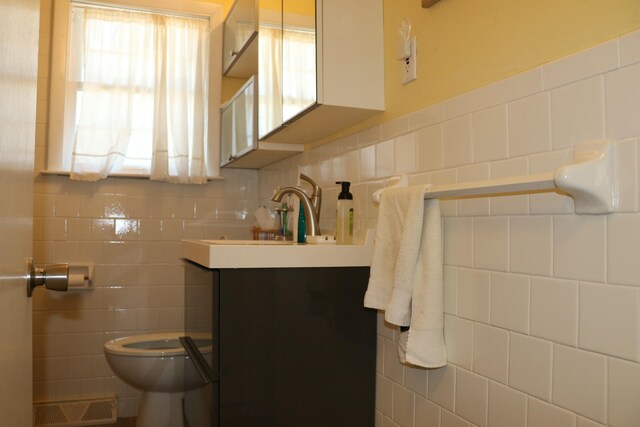 half bath featuring plenty of natural light, vanity, tile walls, toilet, and visible vents