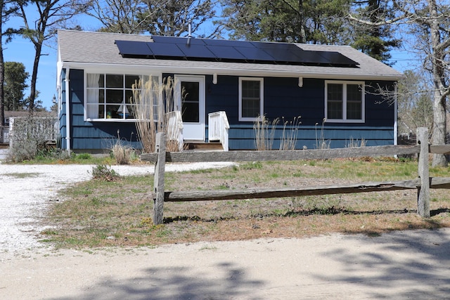 bungalow-style home featuring fence, roof with shingles, and solar panels