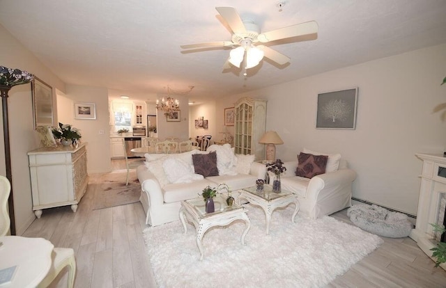 living room featuring ceiling fan with notable chandelier, baseboard heating, a high end fireplace, and light wood-type flooring