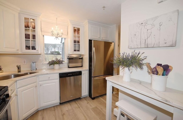 kitchen with appliances with stainless steel finishes, decorative light fixtures, sink, light wood-type flooring, and white cabinetry