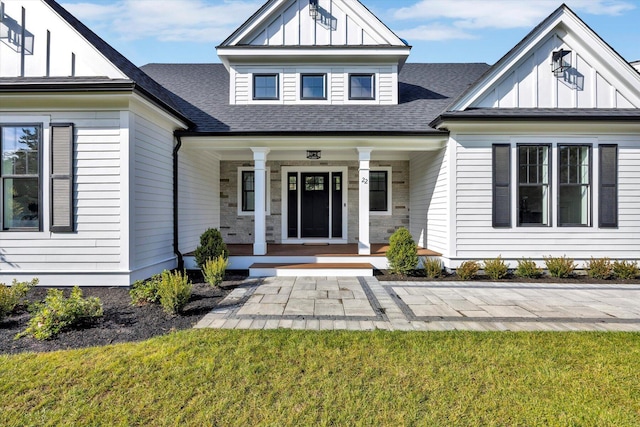 entrance to property with a shingled roof, a porch, board and batten siding, and a yard