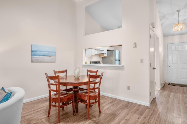 dining room featuring light wood-style flooring, high vaulted ceiling, a chandelier, and baseboards