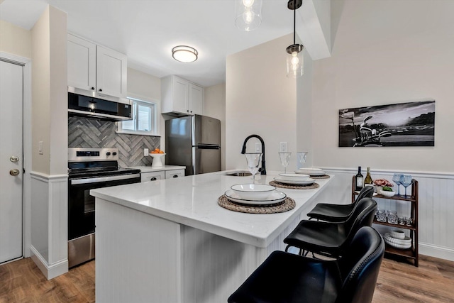 kitchen featuring stainless steel appliances, a sink, light wood finished floors, white cabinetry, and wainscoting