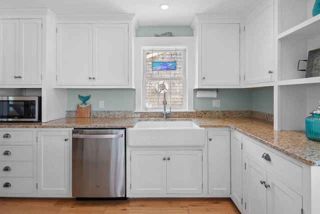 kitchen with appliances with stainless steel finishes, a sink, white cabinetry, light wood finished floors, and light stone counters