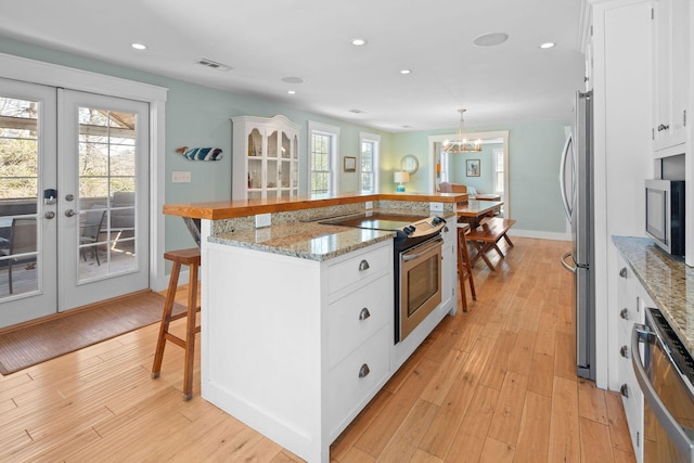 kitchen with stainless steel appliances, a kitchen bar, french doors, light wood-type flooring, and recessed lighting