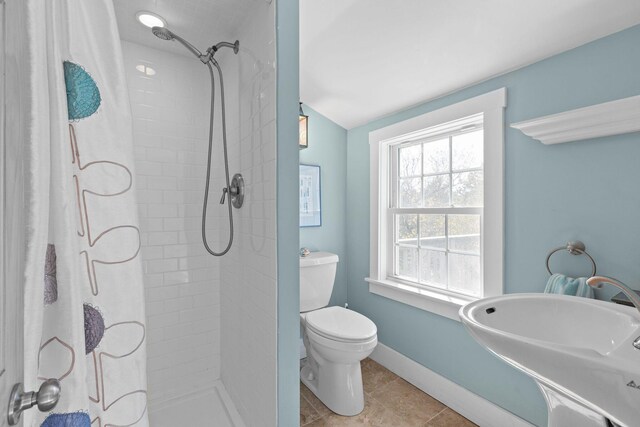 bathroom featuring tiled shower, toilet, a sink, tile patterned flooring, and lofted ceiling