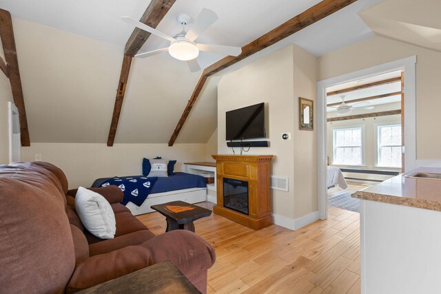 living room featuring a ceiling fan, light wood-style flooring, a glass covered fireplace, and baseboards