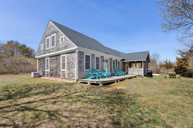 rear view of property featuring a deck, a lawn, and a shingled roof