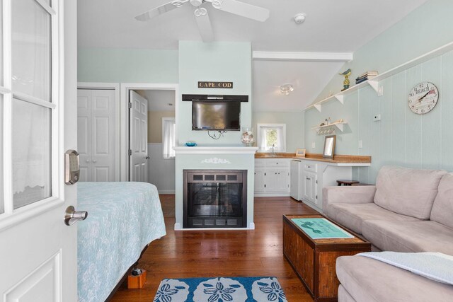 living room featuring dark wood finished floors, ceiling fan, vaulted ceiling, and a glass covered fireplace