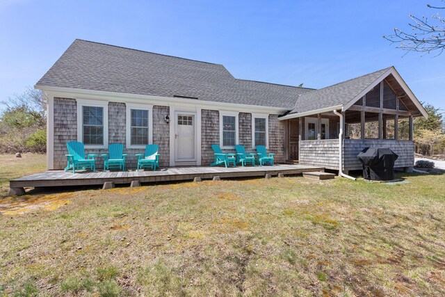 rear view of house featuring a wooden deck, a shingled roof, and a lawn