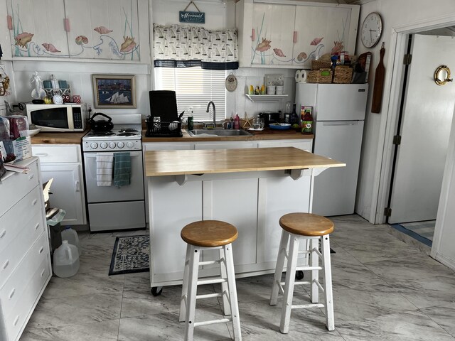 kitchen with white appliances, a kitchen breakfast bar, sink, white cabinets, and butcher block countertops