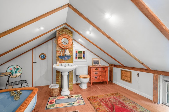 bathroom featuring hardwood / wood-style flooring, a tub to relax in, toilet, and vaulted ceiling