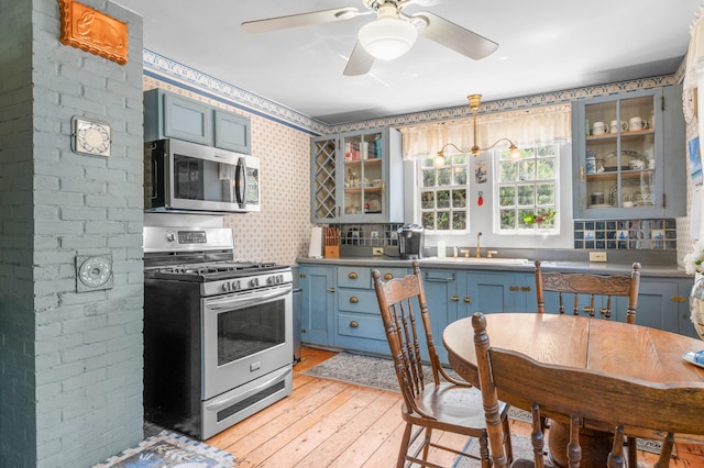 kitchen with appliances with stainless steel finishes, decorative backsplash, blue cabinets, light hardwood / wood-style flooring, and ceiling fan