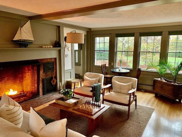 living area featuring beamed ceiling, a baseboard radiator, light hardwood / wood-style floors, and a fireplace