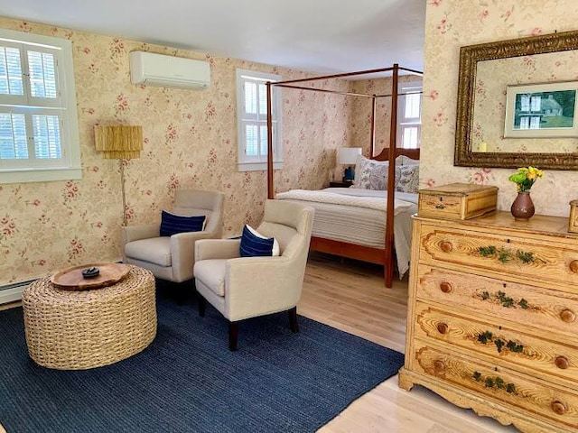 bedroom with a baseboard radiator, hardwood / wood-style floors, and a wall unit AC