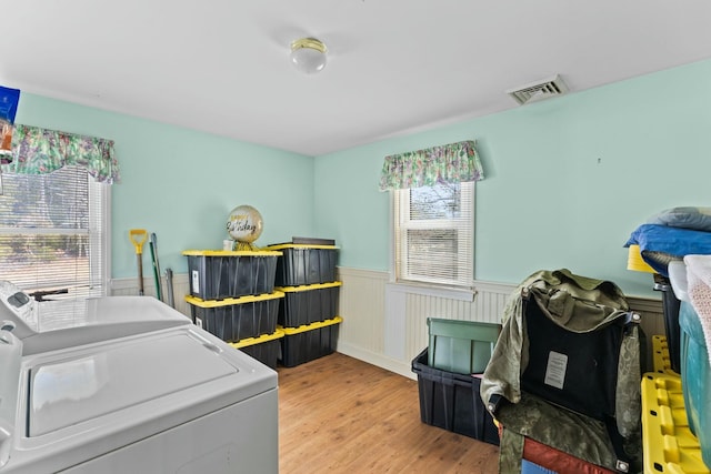 clothes washing area featuring a wainscoted wall, laundry area, wood finished floors, visible vents, and washer and dryer