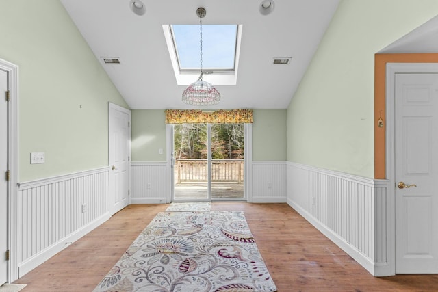 interior space with lofted ceiling with skylight, visible vents, wood finished floors, and wainscoting